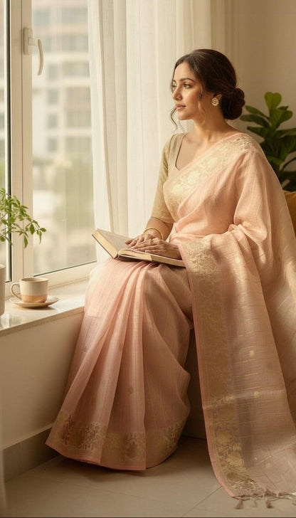 Woman in a peach saree sitting by a window with a book, surrounded by plants.