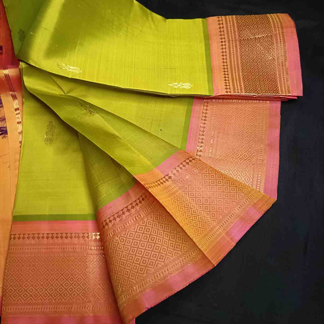 Close-up of orange-pink Mayil Kan peacock eye zari border on parrot green Thirubhuvanam saree